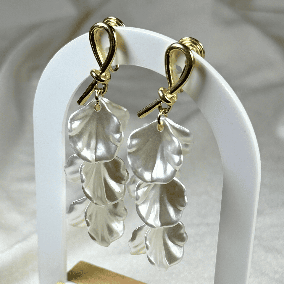 Silver leaf-shaped earrings on a white stand with a soft background