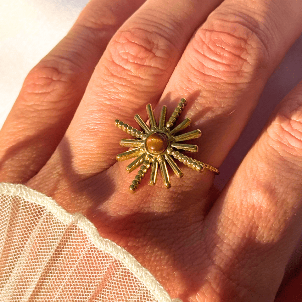 Gold sunburst ring with a brown gemstone on a hand