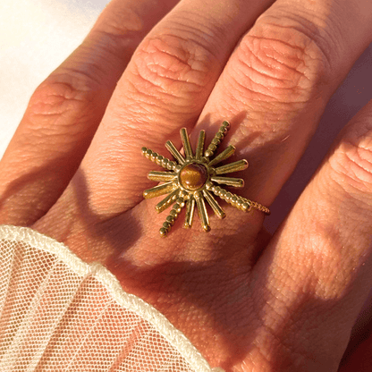 Gold sunburst ring with a brown gemstone on a hand