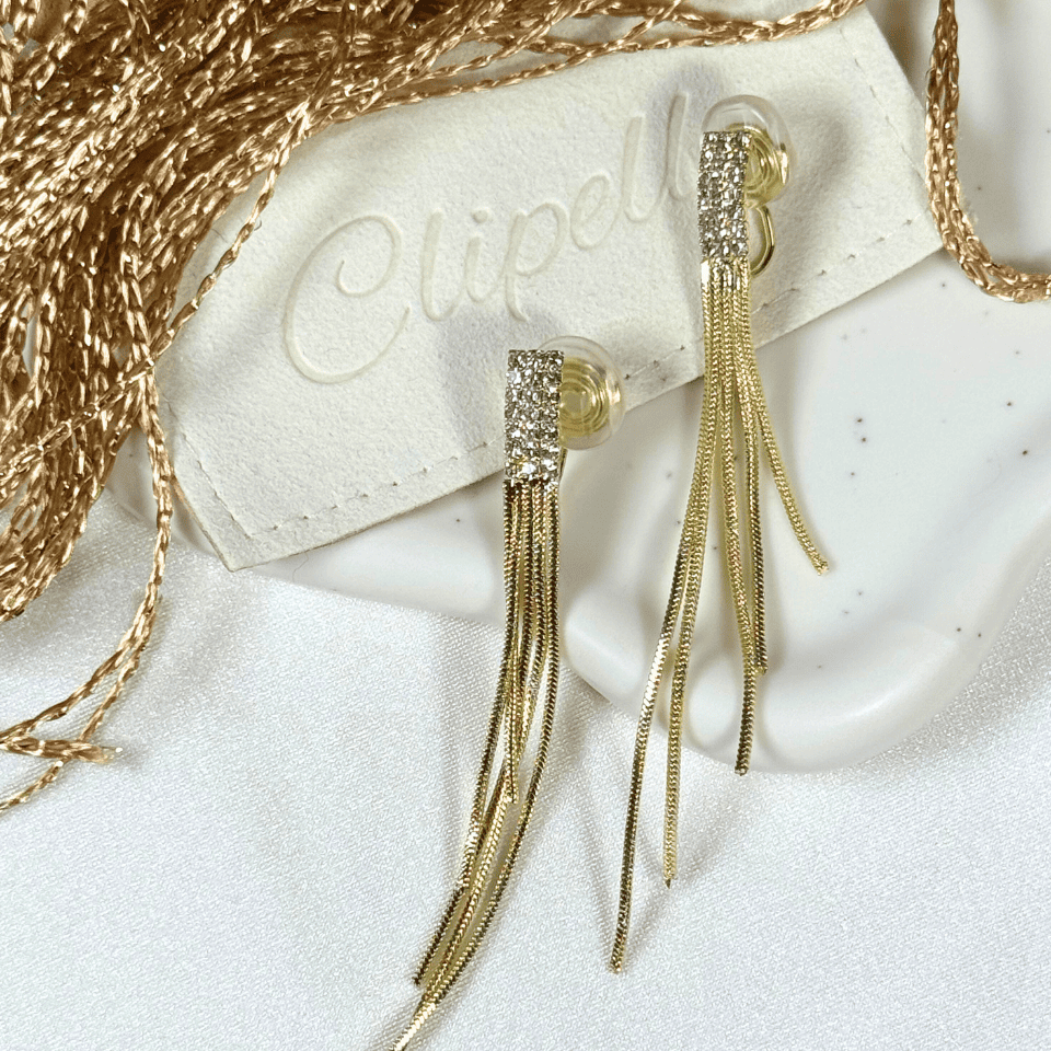 Gold tassel earrings on a white surface with 'Clipelle' branding.
