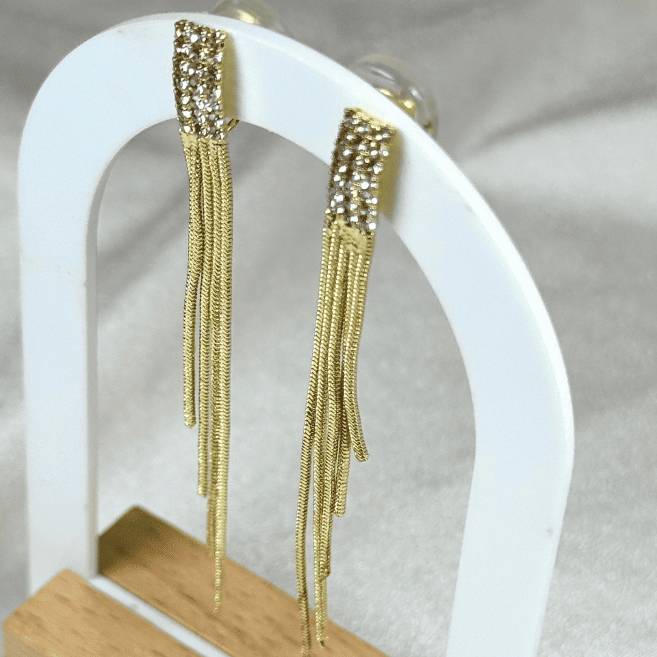 Gold fringe earrings on a white stand with a neutral background