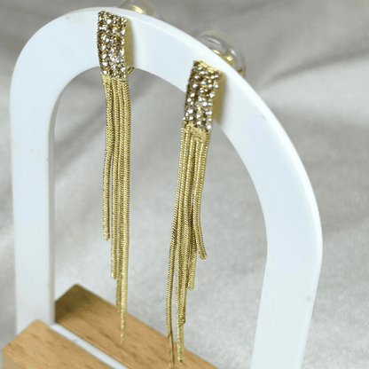 Gold fringe earrings on a white stand with a neutral background