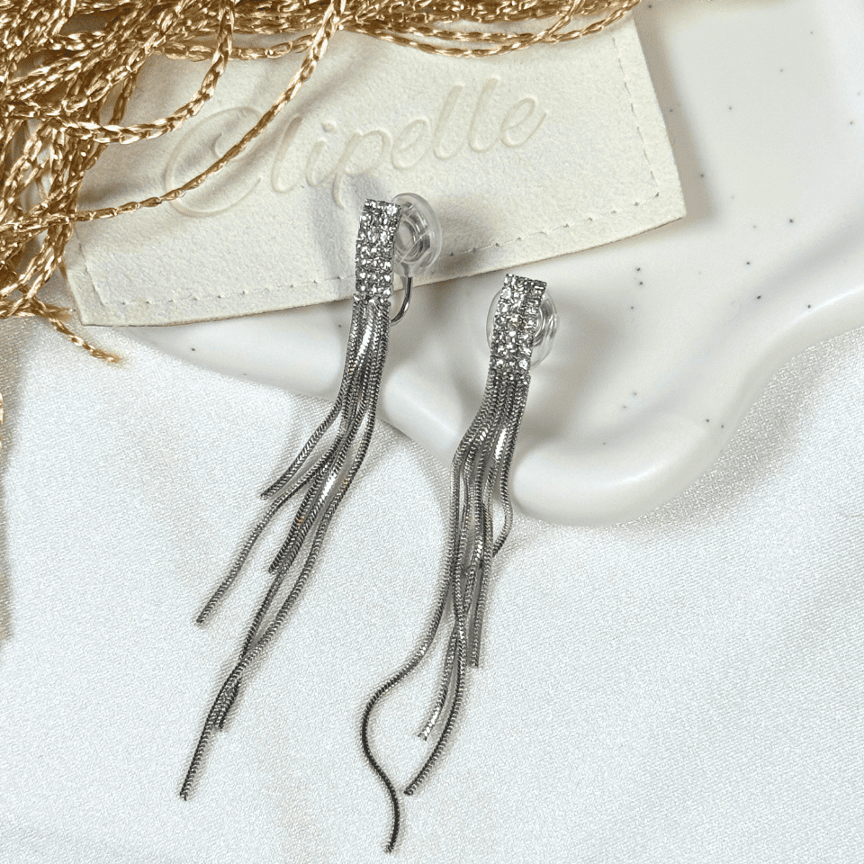 Silver tassel earrings on a white surface with a branded card in the background