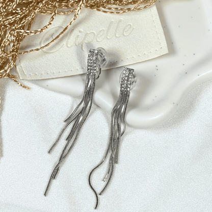 Silver tassel earrings on a white surface with a branded card in the background