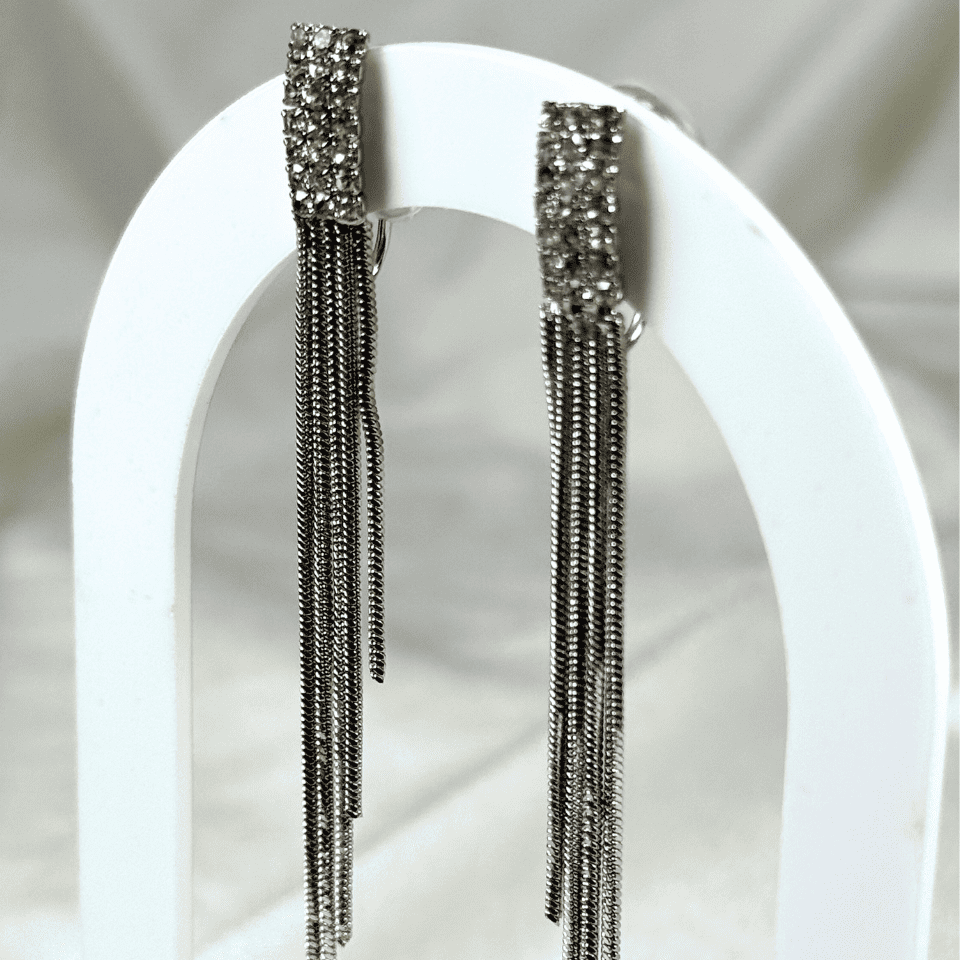 Pair of silver fringe earrings on a white stand with a neutral background