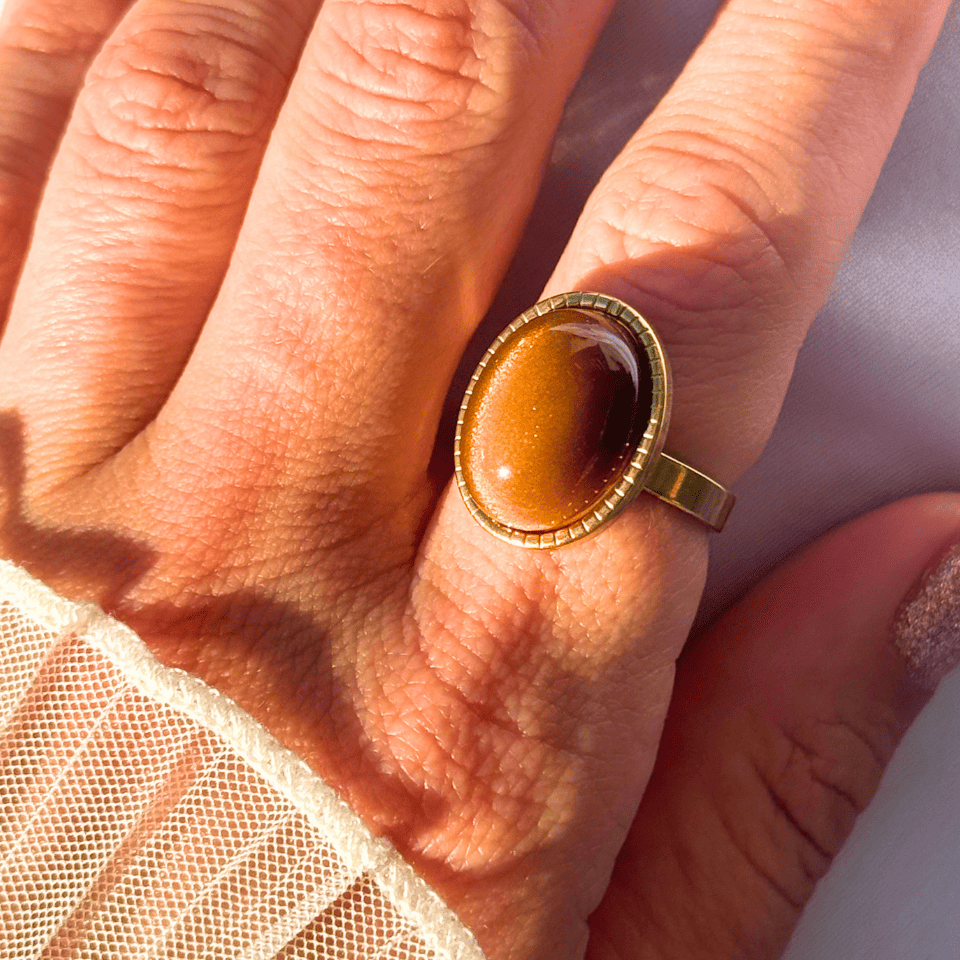 Close-up of a hand wearing a gold ring with a brown stone.