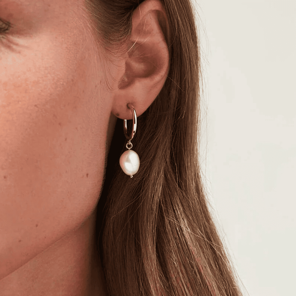 Close-up of a woman wearing a pearl earring with a plain background