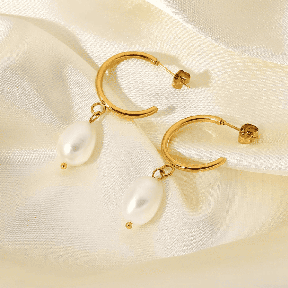 Gold hoop earrings with pearl drops on a satin surface