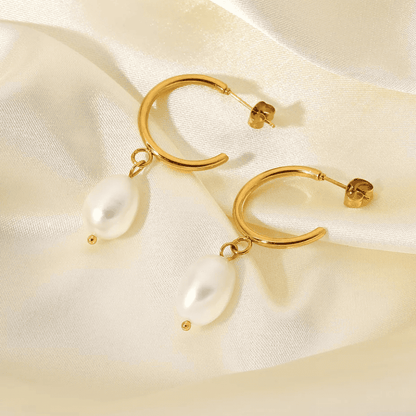Gold hoop earrings with pearl drops on a satin surface