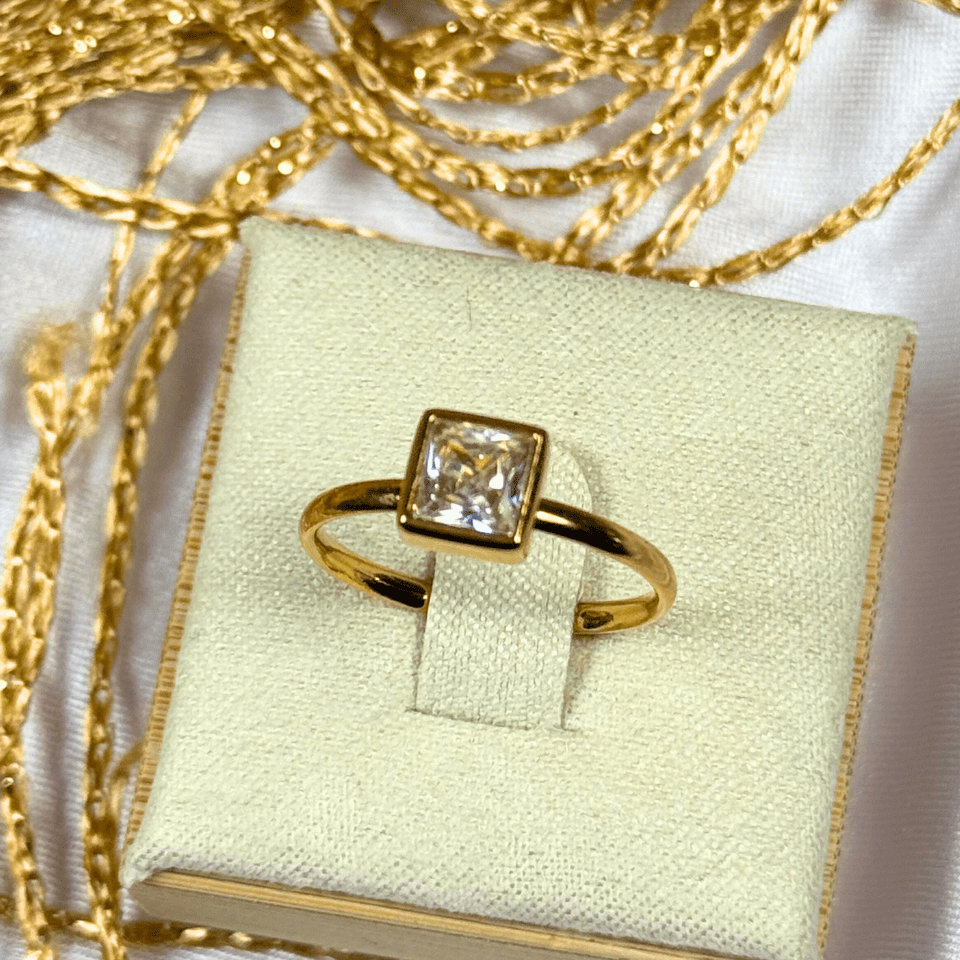 Gold ring with a diamond on a light green jewelry box with gold chains.