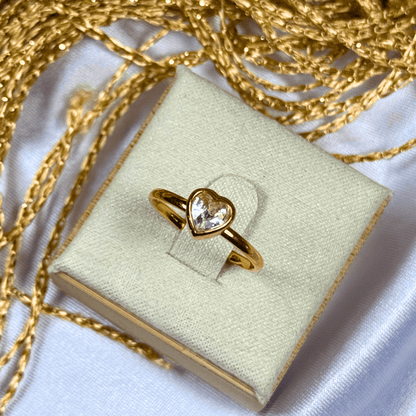 Gold heart-shaped ring on a light green jewelry box with gold chain in the background
