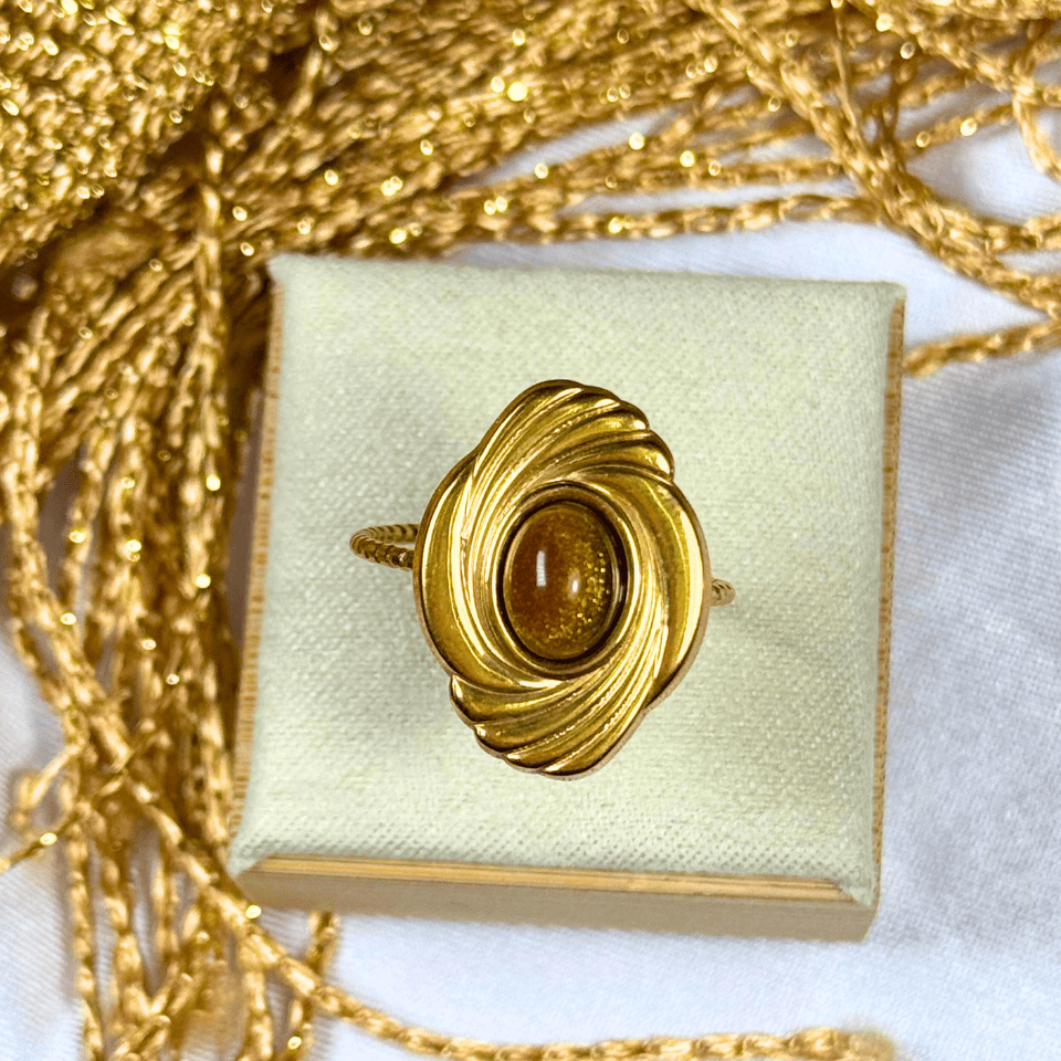 Gold ring with a central gemstone on a white box with gold chain