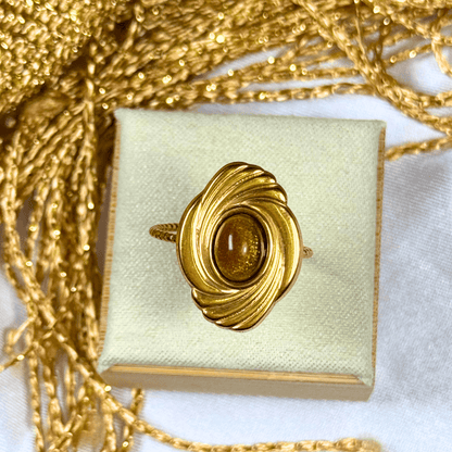 Gold ring with a central gemstone on a white box with gold chain