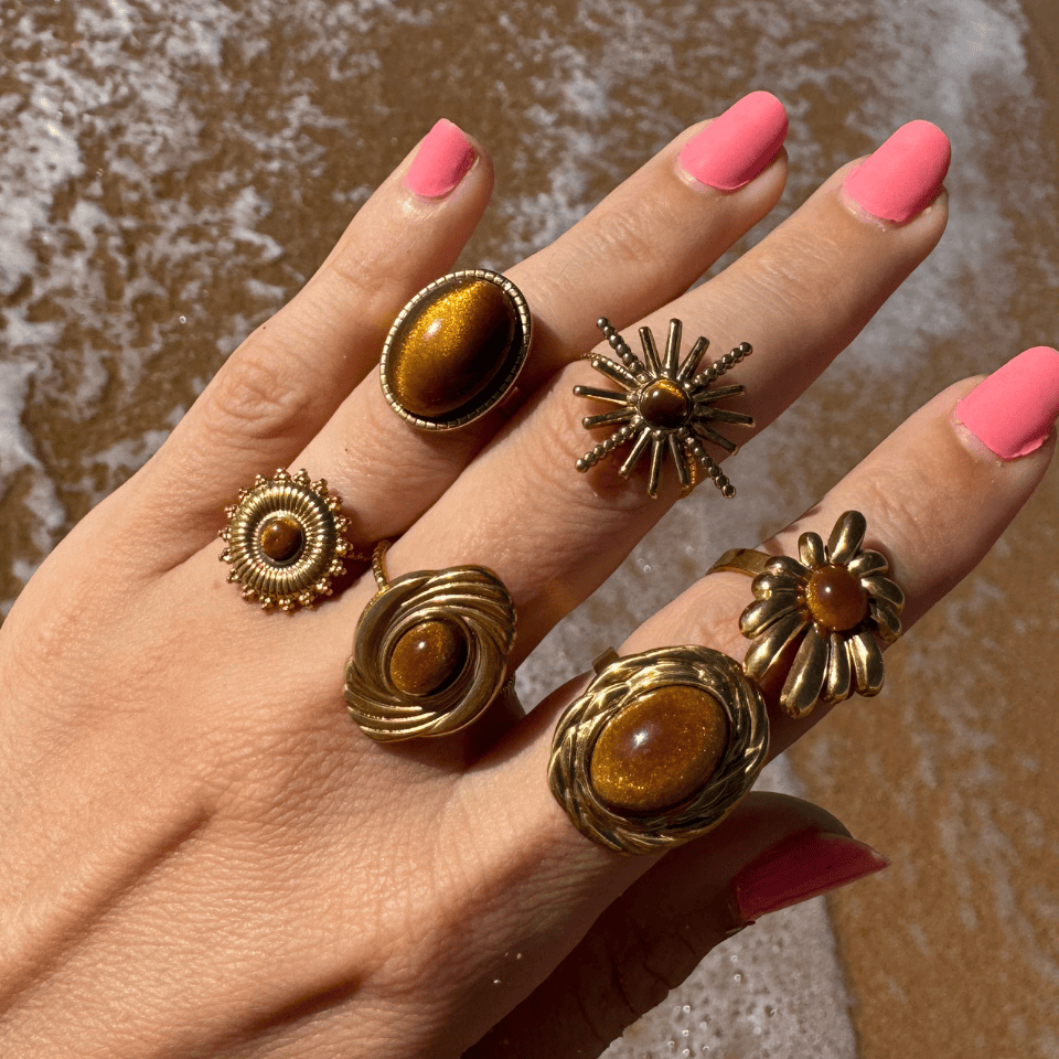 Hand wearing multiple gold rings with brown stones against a blurred background