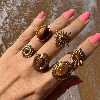 Hand wearing multiple gold rings with brown stones against a blurred background